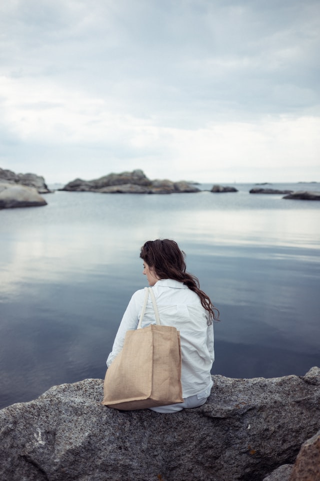 Jente som sitter med ryggen til og ser ut over havet